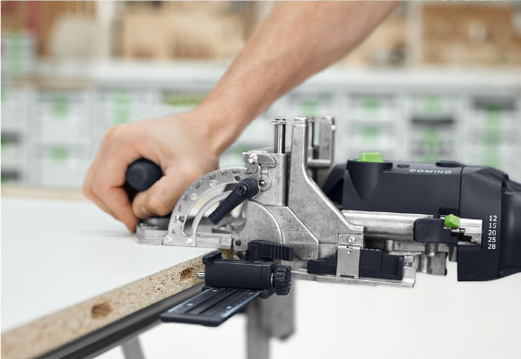 Close-up of a person operating a precision power tool to cut or shape the edge of a wooden board in a workshop setting.