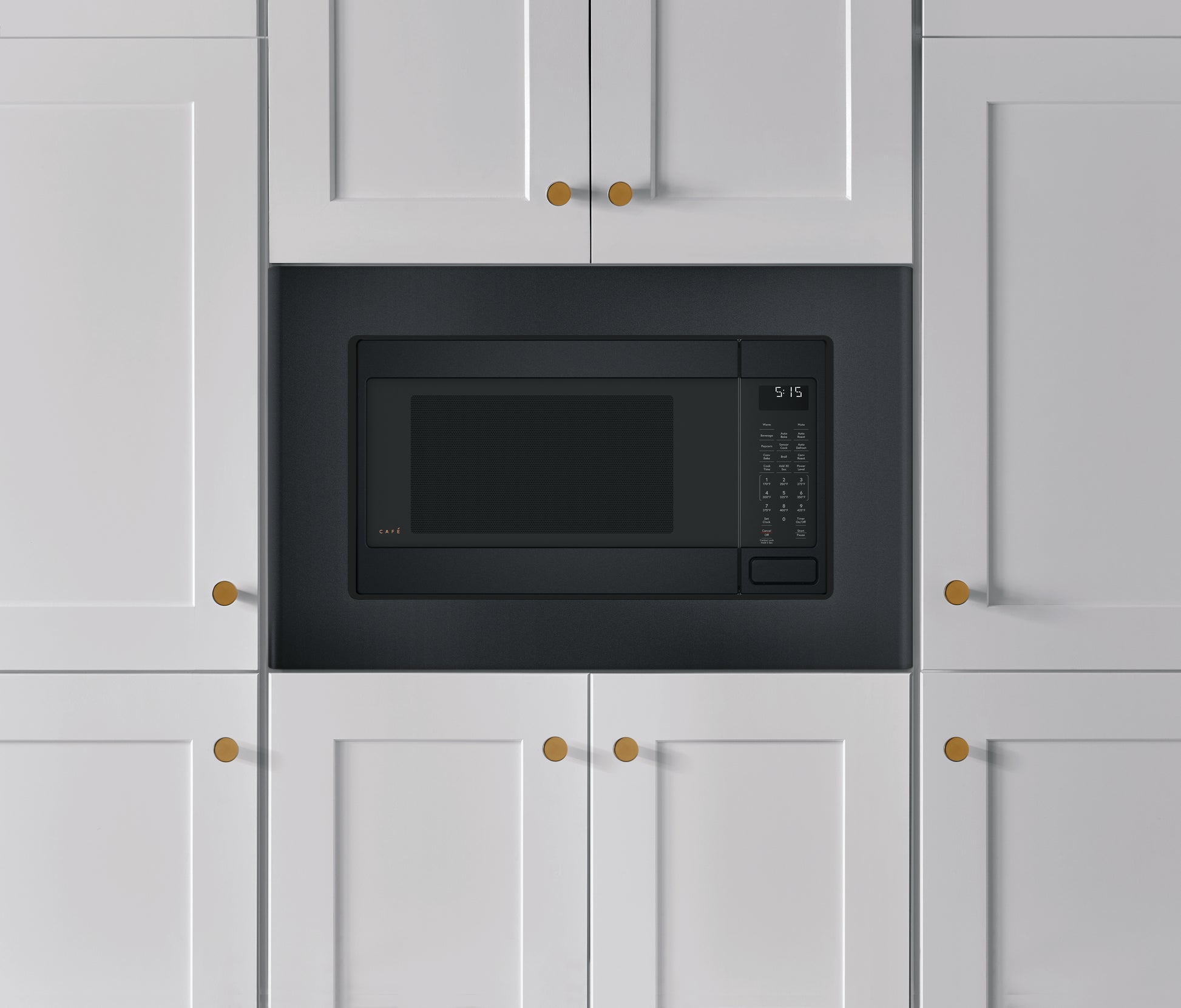 Matte black built-in trim kit surrounding a microwave installed in white kitchen cabinetry with brass hardware handles