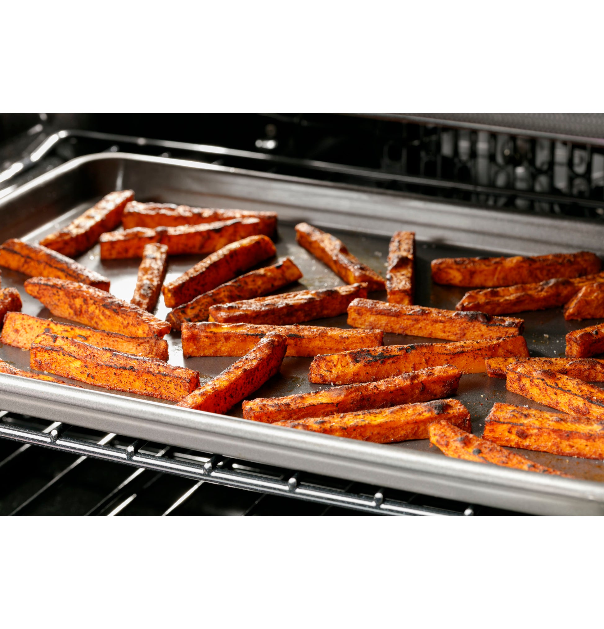 Sweet potato fries roasting on a metal pan inside a dual-fuel range oven from kitchen appliance collection