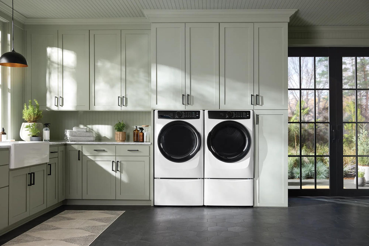 Pair of white front load washers with black doors in modern kitchen featuring gray cabinetry and large glass doors
