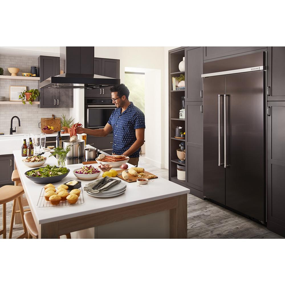 Man cooking in modern kitchen with dark cabinetry, black appliances, and prepared dishes on white island countertop