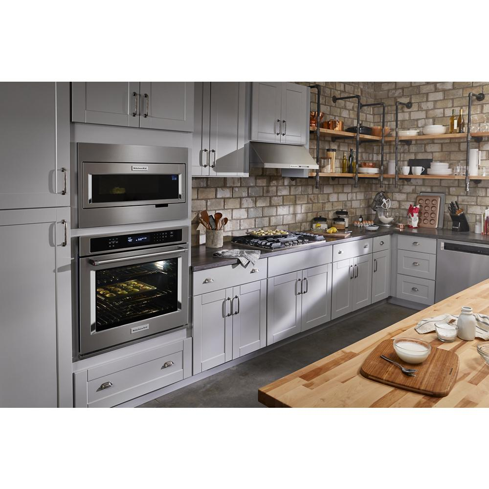 Contemporary kitchen with gray cabinetry, stainless steel appliances, brick backsplash, wooden shelves, and butcher block island