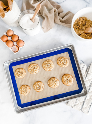 Half sheet pan with blue-bordered silicone baking mat holding freshly baked cookies on marble countertop in kitchenware setting