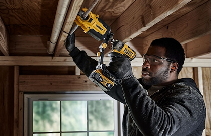 Worker wearing safety glasses using a DEWALT impact tool with copper pipe cutter attachment for plumbing tasks