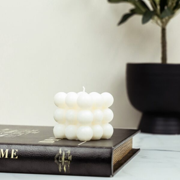 White square bubble candle placed on a hardcover book next to a black planter with a small plant