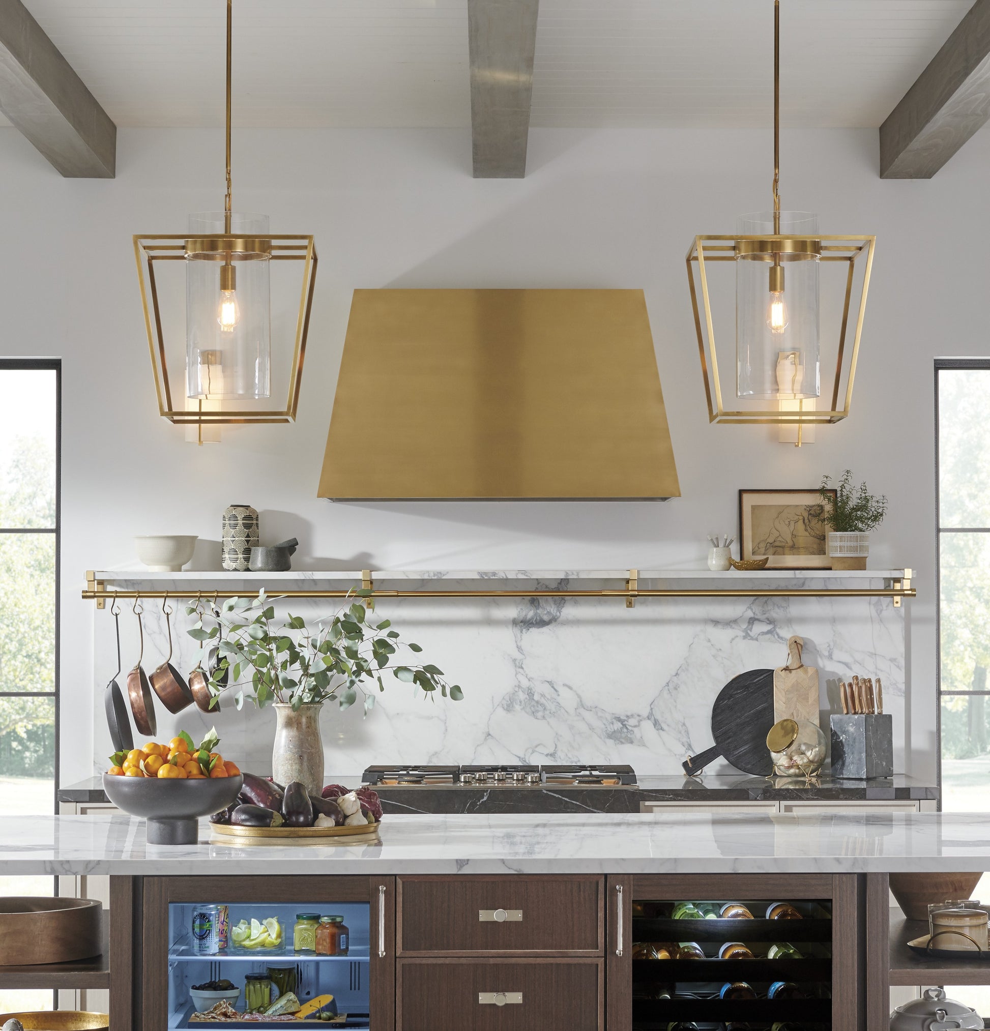 Custom brass range hood above marble backsplash in kitchen with pendant lighting and cookware in home improvement collections