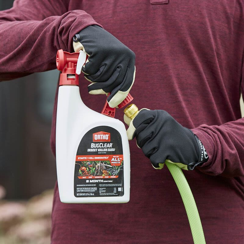 Person wearing gloves attaching red and white insect killer spray to green garden hose for outdoor pest control