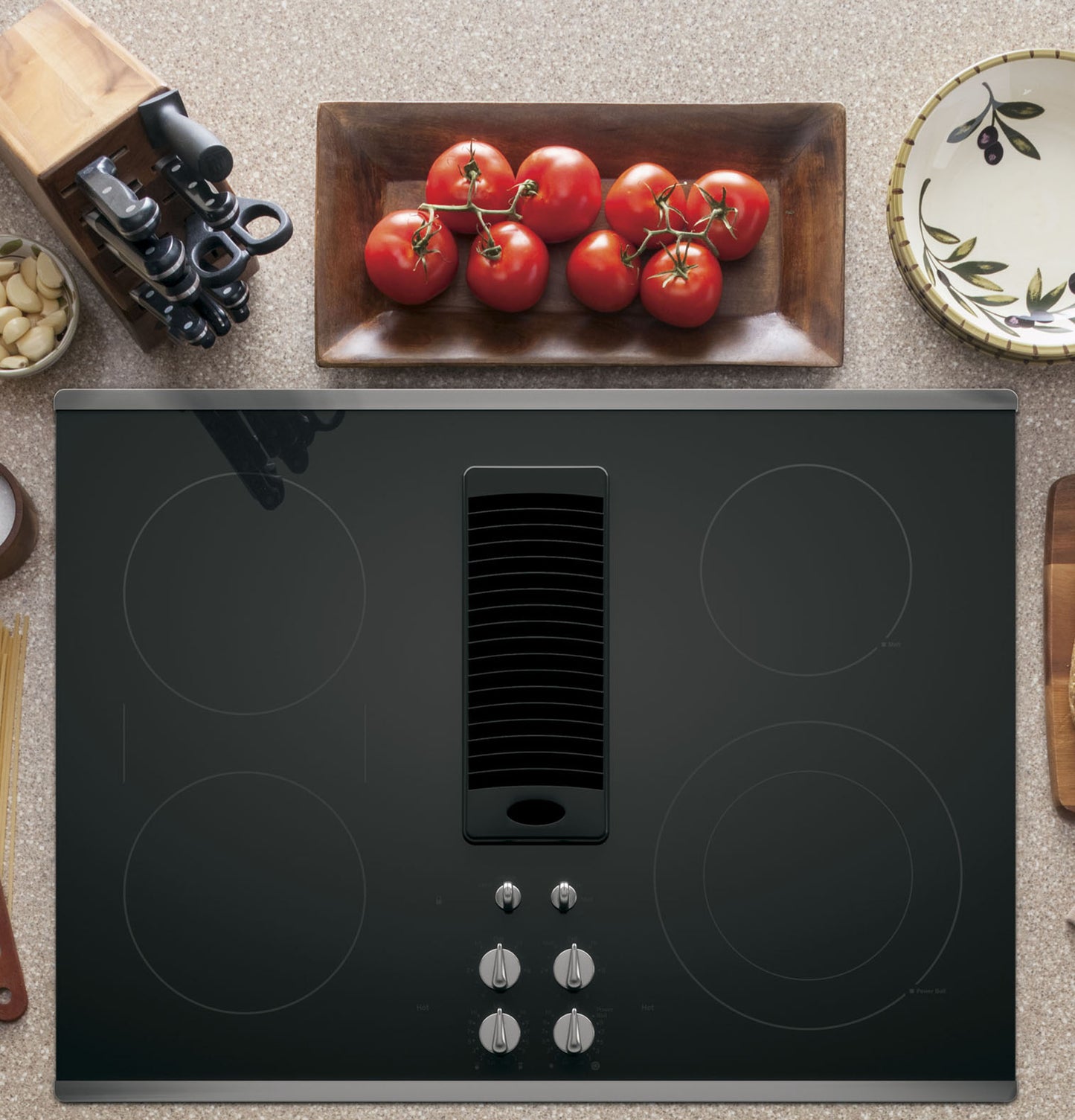 Black electric downdraft cooktop with four radiant elements and control knobs, styled in home kitchen setting
