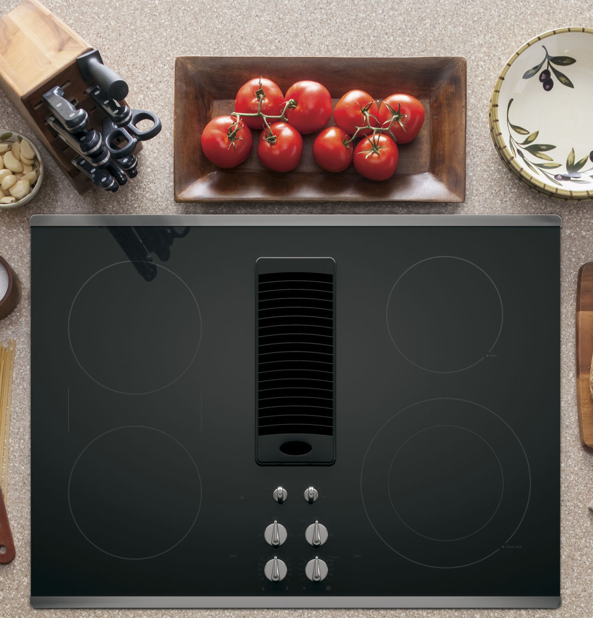 Black electric downdraft cooktop with four radiant elements and control knobs, styled in home kitchen setting