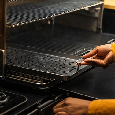 Hand placing stainless steel grill tray with perforated surface into outdoor grill for grilling fish and vegetables
