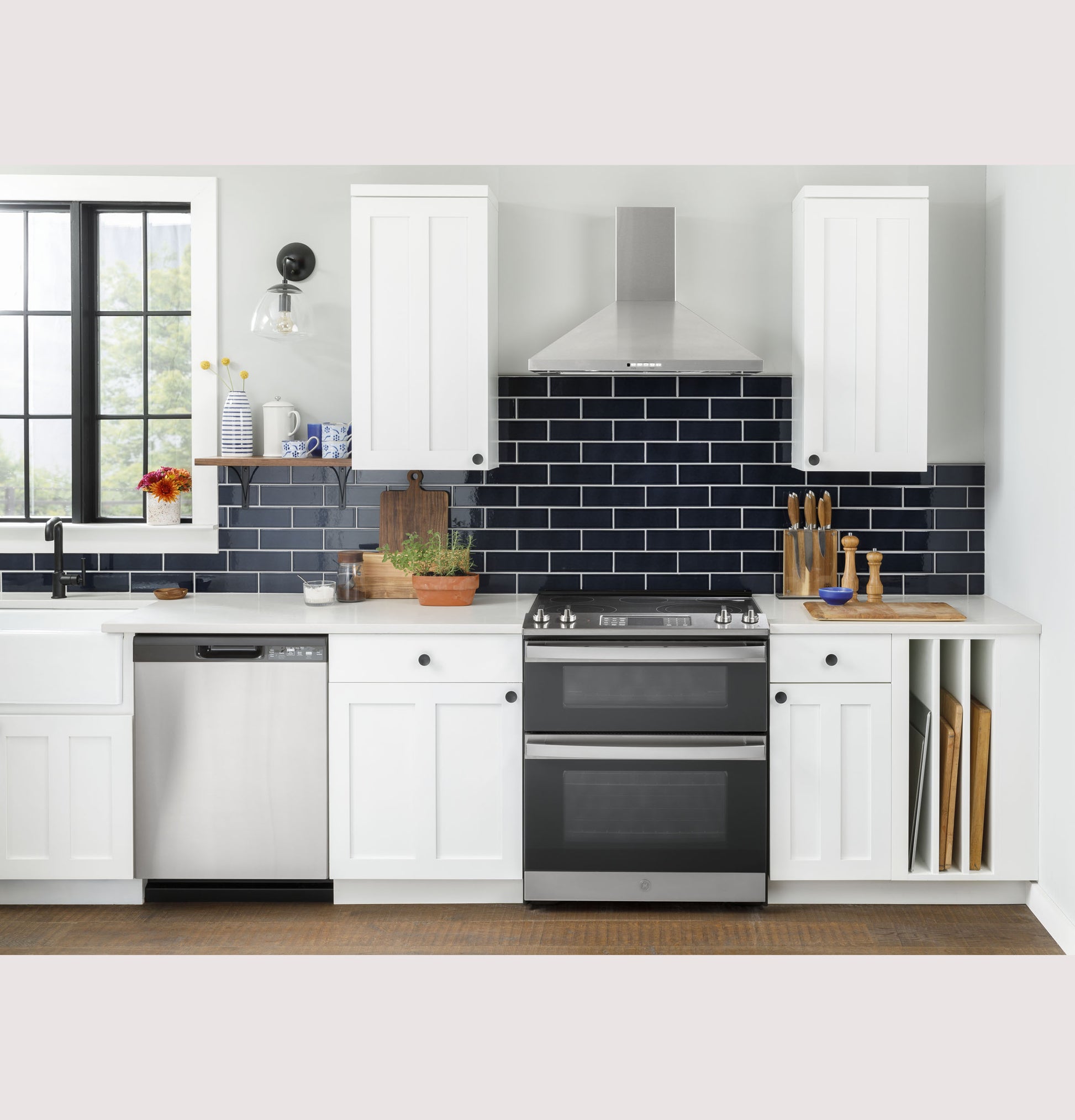 Modern kitchen scene with stainless steel slide-in electric convection double oven range, white cabinetry, and dark tile backsplash