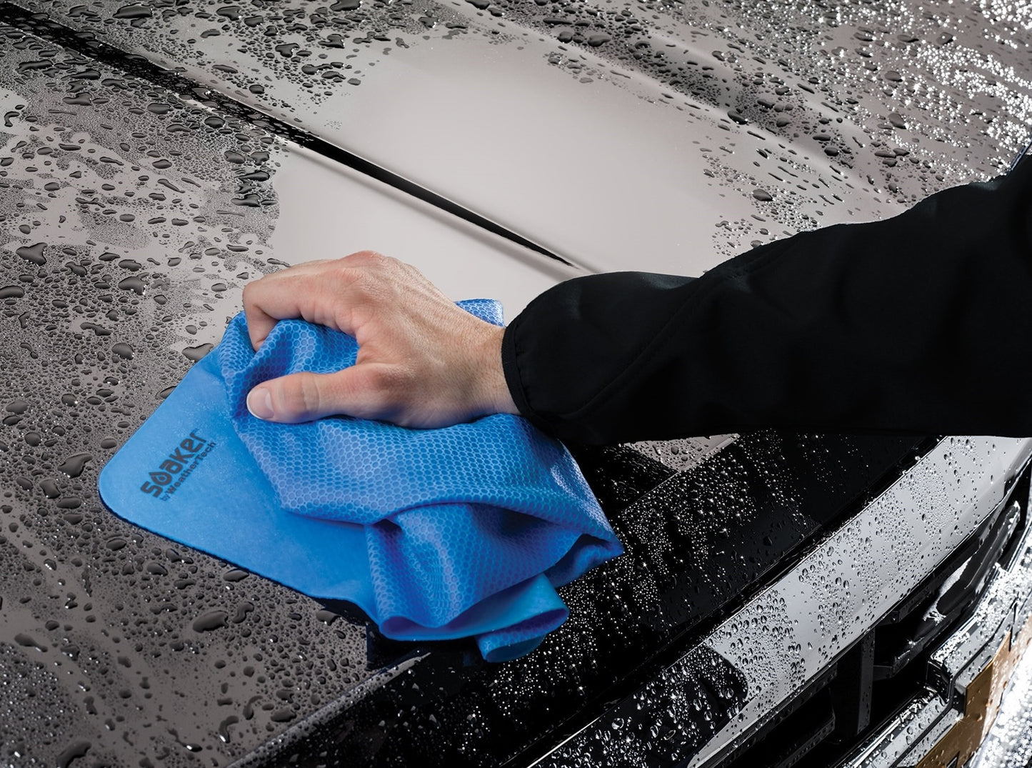 Hand using blue reusable drying towel to wipe water droplets off black vehicle surface in automotive accessory setting