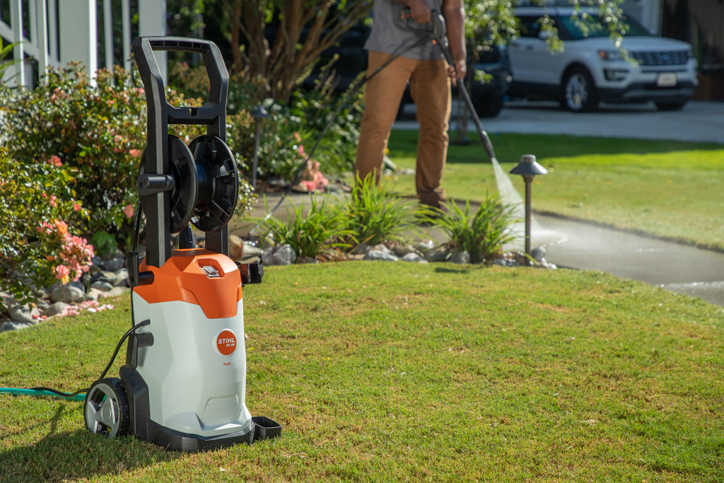 STIHL RE 90 Plus pressure washer with hose reel and wheels on lawn being used for outdoor cleaning tasks