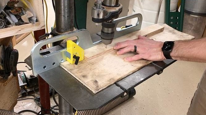 Adjustable metal drill press fence with yellow magnetic stops securing wood for precise drilling in power tool accessories collection