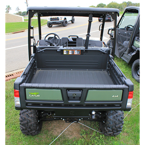 Rear view of green John Deere utility vehicle with cargo bed and off-road tires parked on grass near road