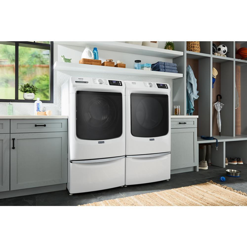 Pair of white front load washers and dryers with pedestal drawers in organized laundry room with gray cabinetry and shelves