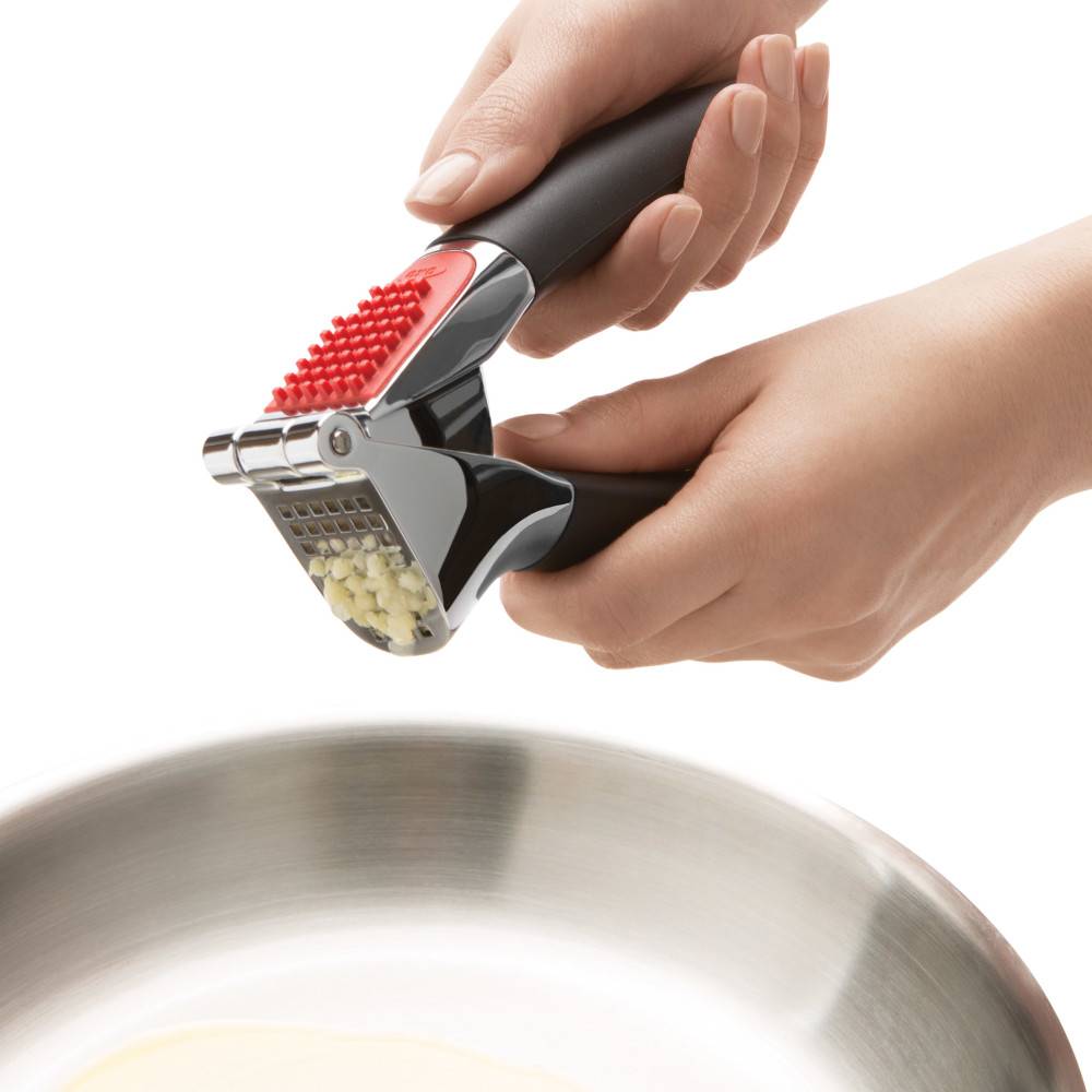 Hands pressing fresh garlic cloves with metal chamber and black handles for kitchenware and home tools under $50 collections