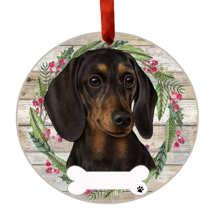 Round Christmas ornament with a black dachshund portrait framed by a festive wreath and red hanging ribbon