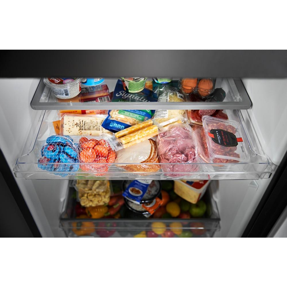 Clear refrigerator drawer filled with assorted deli meats, cheeses, packaged snacks, and fresh produce inside top freezer fridge compartment
