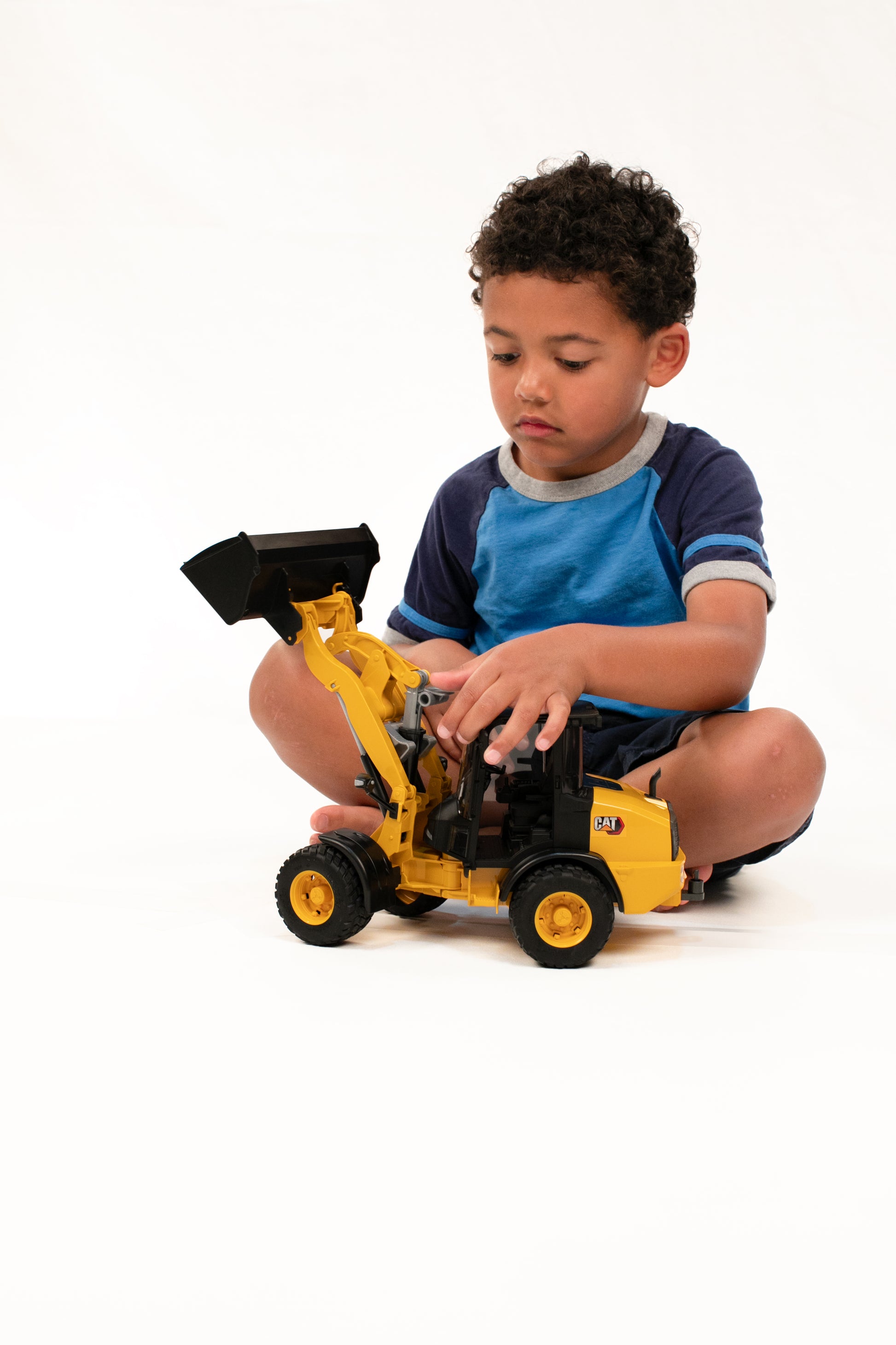 Young child focused on playing with yellow Bruder CAT wheel loader toy in a home improvement play setting