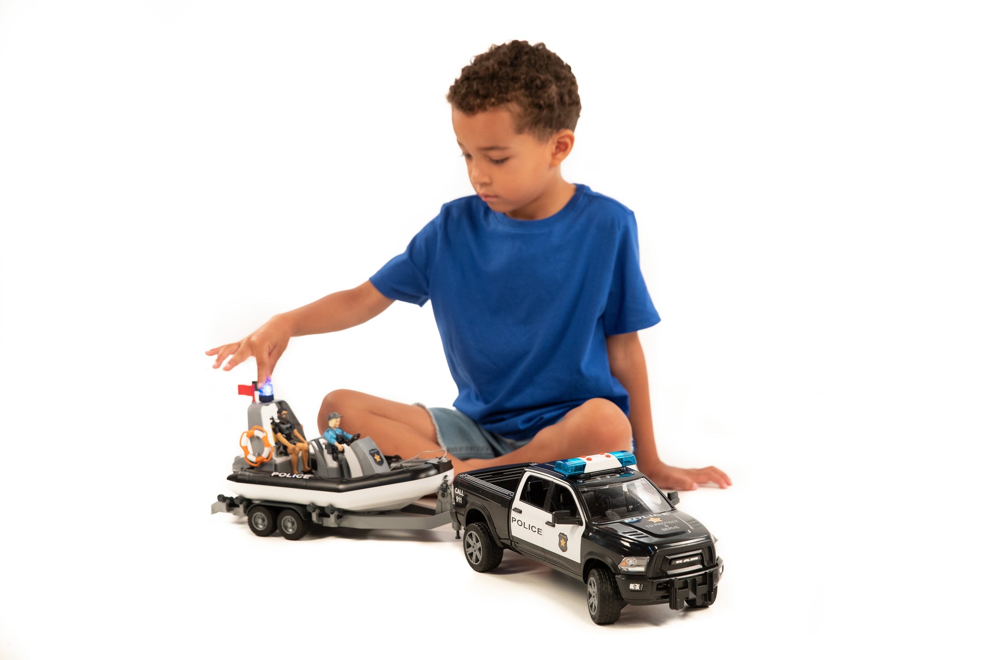 Child playing with black and white police pickup toy towing a trailer with a patrol boat and two figures