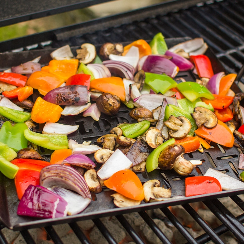 Seasoned carbon steel grilling pan with mixed colorful vegetables cooking outdoors on a barbecue grill in a home improvement setting