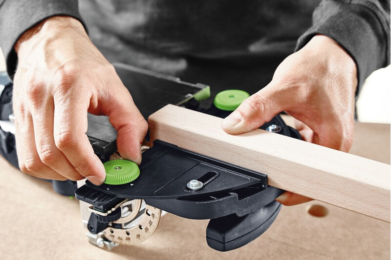 Hands adjusting green knob on black Festool tool accessory securing narrow wooden rail for woodworking precision