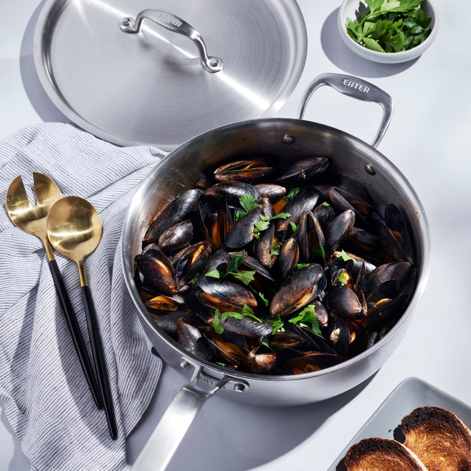 Fully clad stainless steel 4-quart saute pan with lid filled with cooked mussels in kitchenware collection