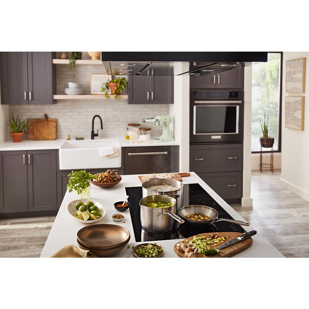 Modern kitchen with gray cabinets featuring a 30-inch induction cooktop cooking multiple pots and fresh ingredients nearby