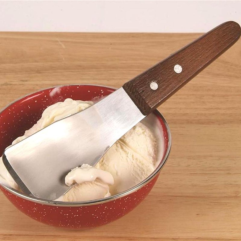 Stainless steel ice cream spade with riveted hardwood handle resting on creamy vanilla ice cream in red speckled bowl