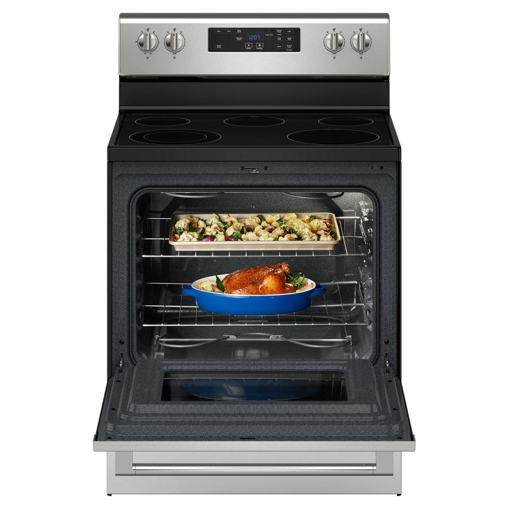 Open electric range oven with baked chicken in blue baking dish and roasted vegetables on top rack for kitchenware