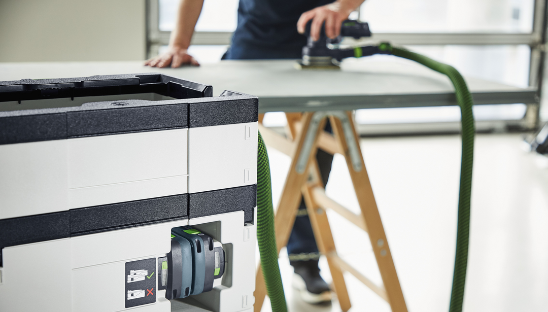 Cordless HEPA dust extractor with green hose connected to power tool for woodworking tools and air filtration collection