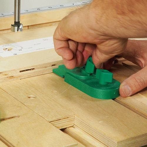Hand tightening green plastic ramp clamp on wood surface for precise woodworking and home improvement tasks