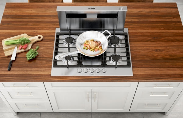 36-inch stainless steel gas cooktop with five burners and a frying pan cooking vegetables on wooden countertop
