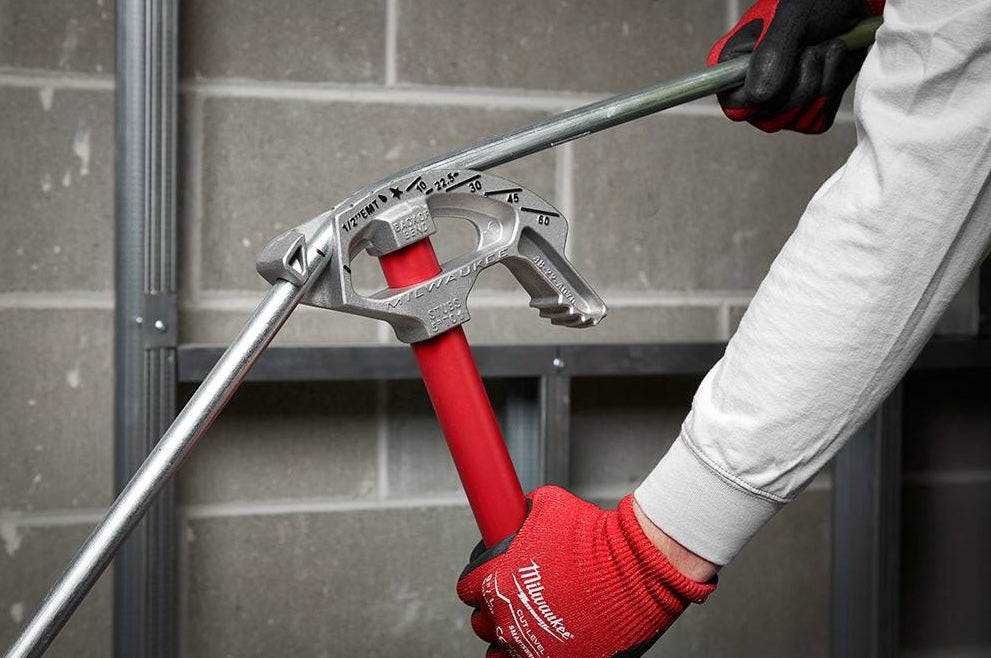 Worker using red-handled aluminum conduit bender to shape metal EMT conduit in a home improvement setting
