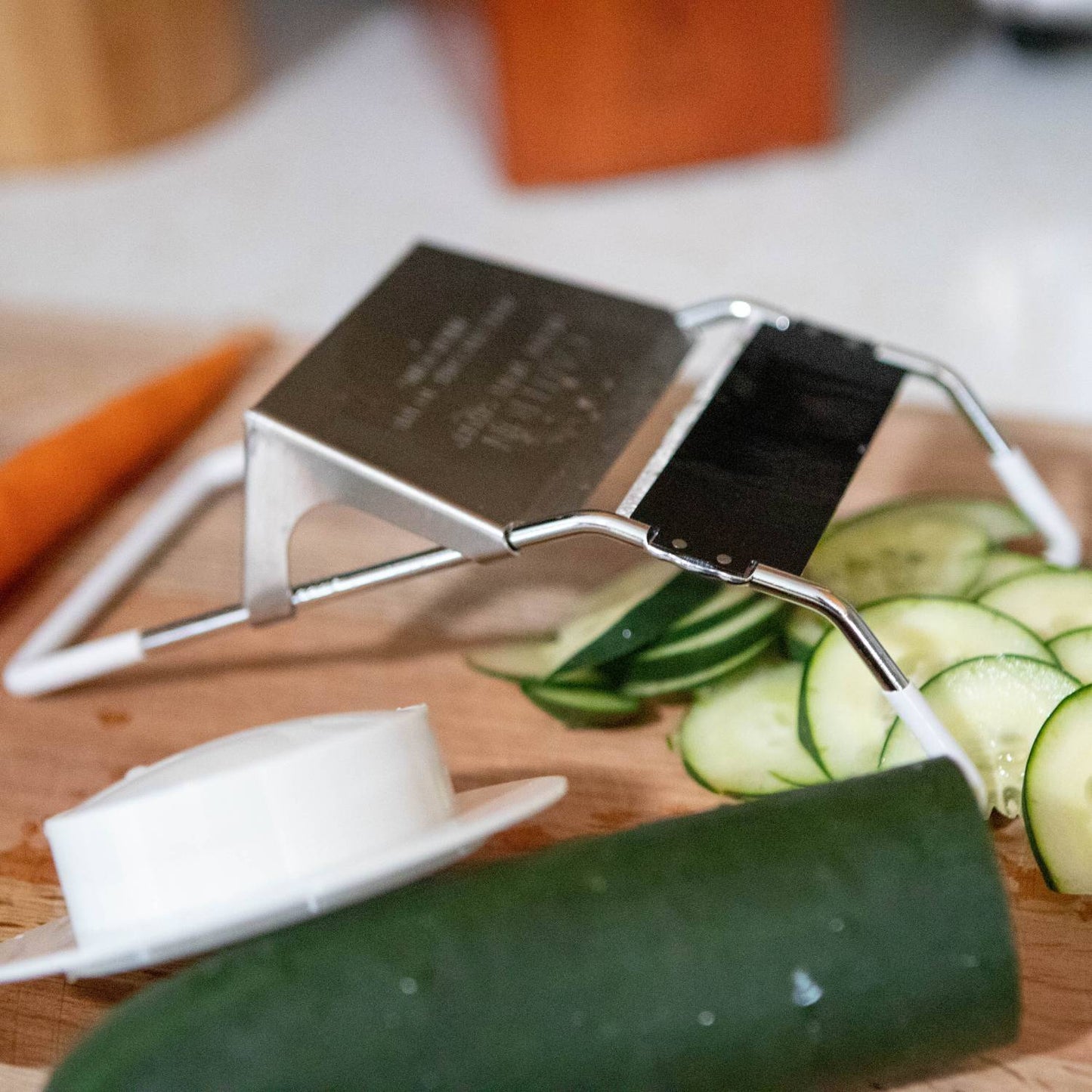 Stainless steel vegetable slicer with black blade and white hand guard on wooden cutting board in kitchenware collection