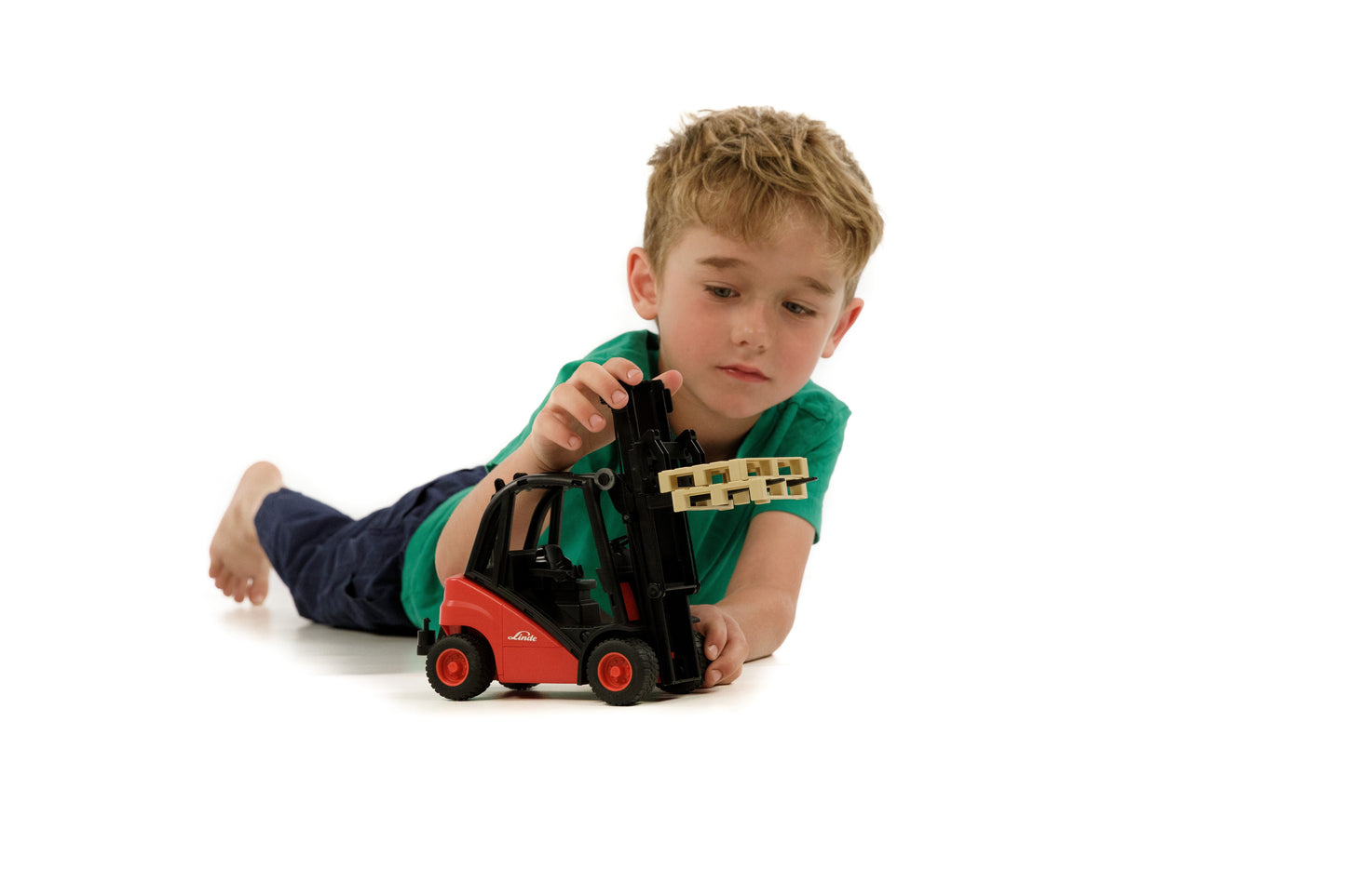 Child lying down playing with red and black Bruder stacker toy lifting a wooden pallet in toys and games collection