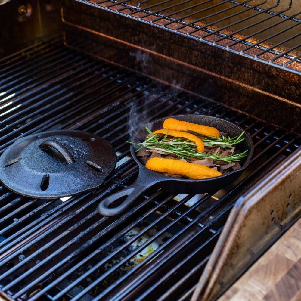 Cast iron smoker skillet with vented lid open on grill with smoking herbs and orange wood chips in kitchenware collections
