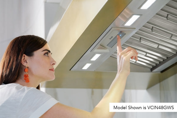 Woman adjusting controls on stainless steel custom insert range hood in modern kitchen setting