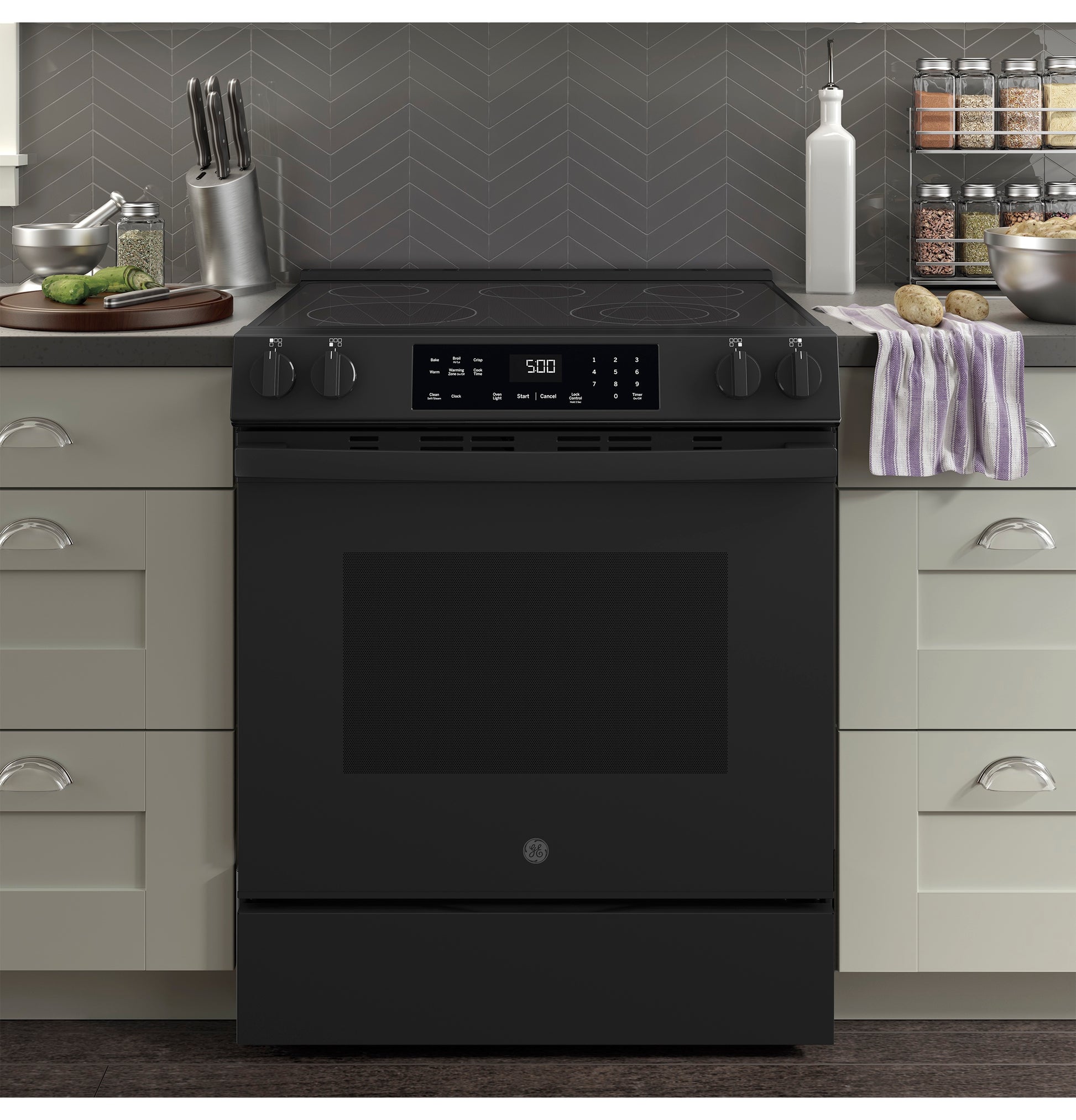 Black slide-in electric range with digital display and control knobs set in modern kitchen with gray cabinetry and countertop accessories