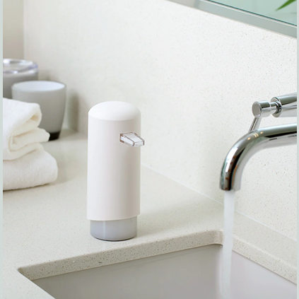 White foaming soap dispenser with clear pump placed on bathroom counter near modern faucet and towels in bath setting