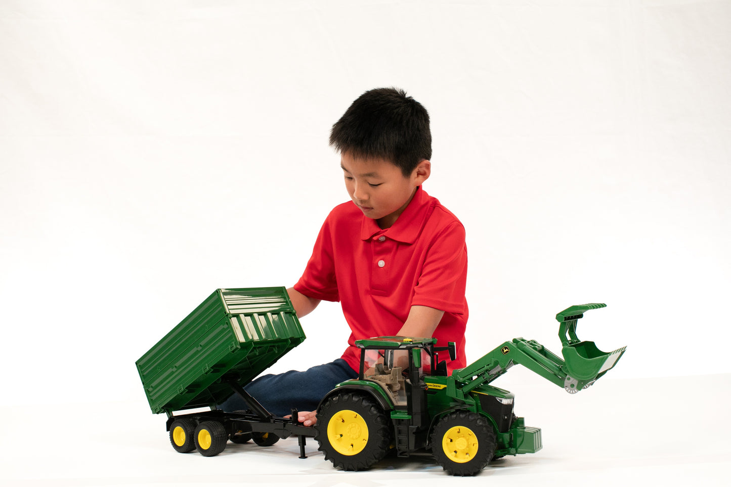 Child playing with green John Deere toy tractor featuring front loader and tipping trailer for creative farm play sets