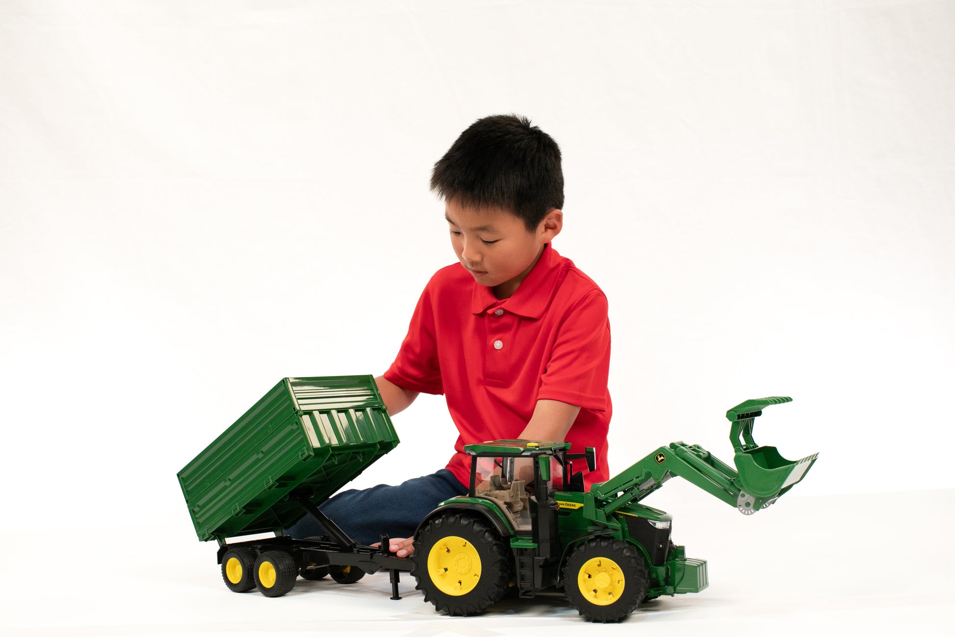 Child playing with green John Deere toy tractor featuring front loader and tipping trailer for creative farm play sets