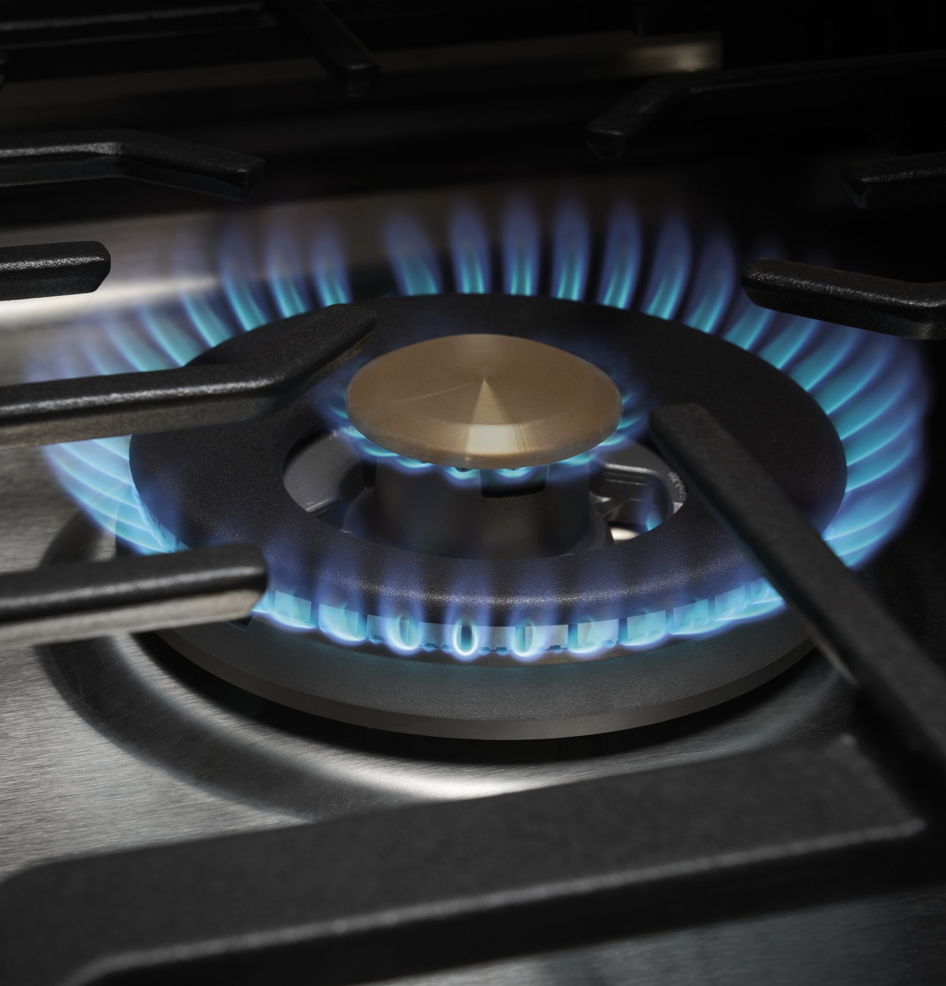 Close-up of gas burner flame glowing blue on stainless steel recessed cooktop in modern kitchen appliance setting