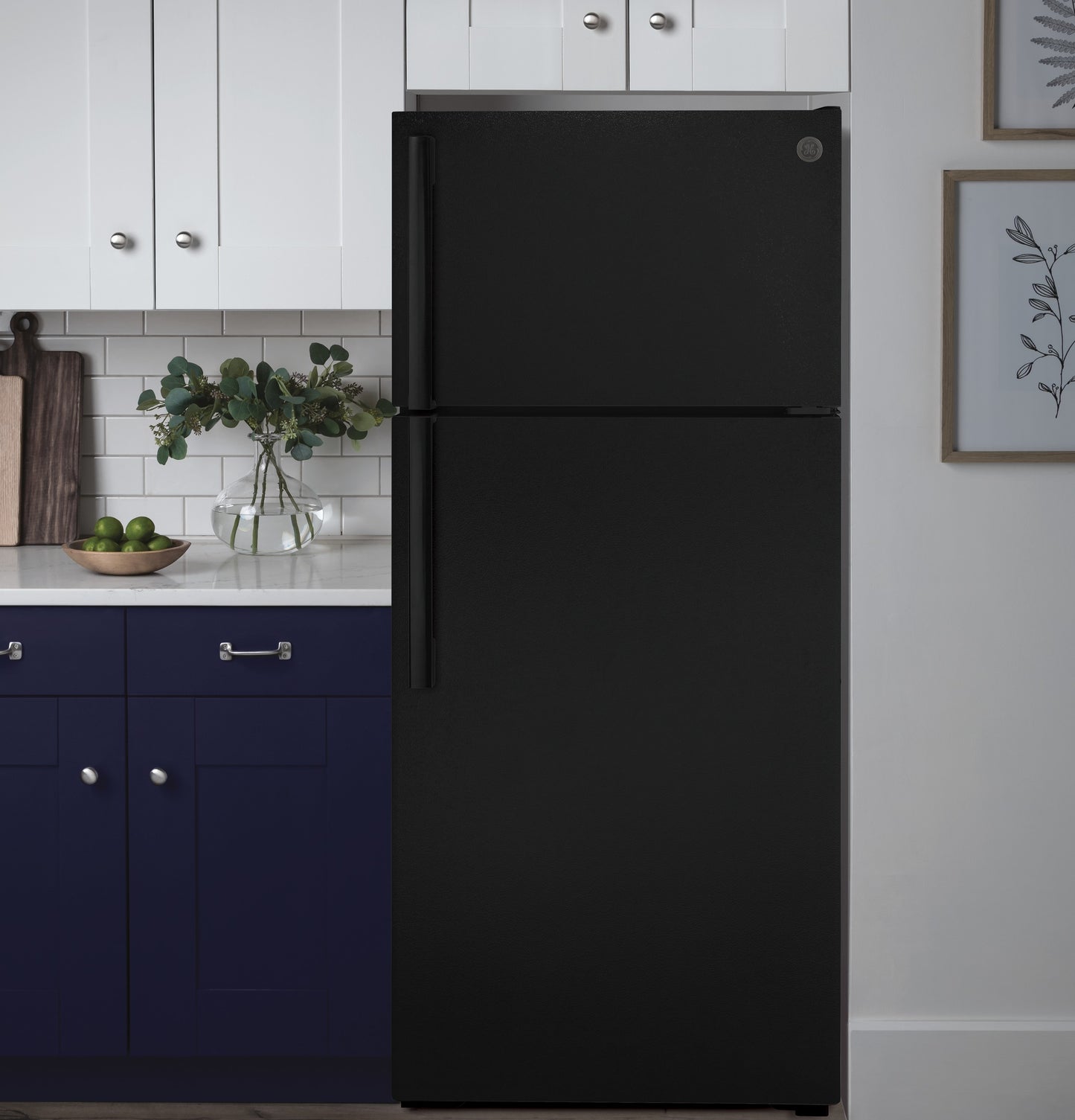 Matte black top-freezer refrigerator in a modern kitchen with white and navy blue cabinetry and simple decor