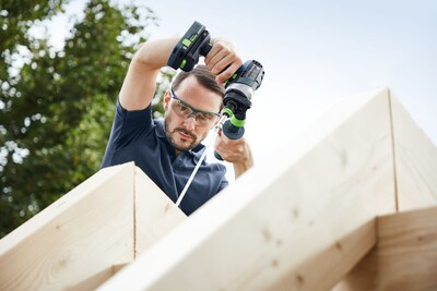 Man wearing safety glasses using cordless drill to assemble large wooden beams during home improvement project