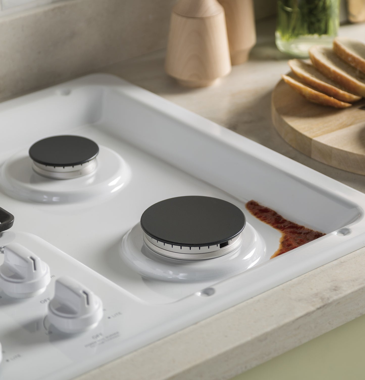 Close-up of white gas cooktop burner with spilled sauce near dishwasher-safe grates in kitchenware collection