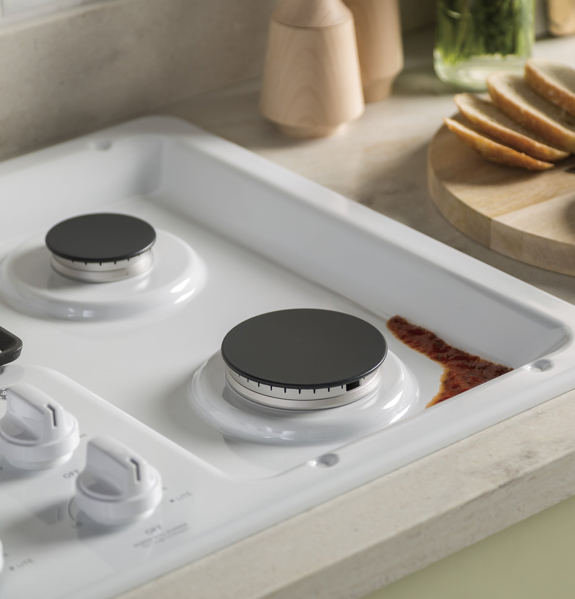 Close-up of white gas cooktop burner with spilled sauce near dishwasher-safe grates in kitchenware collection