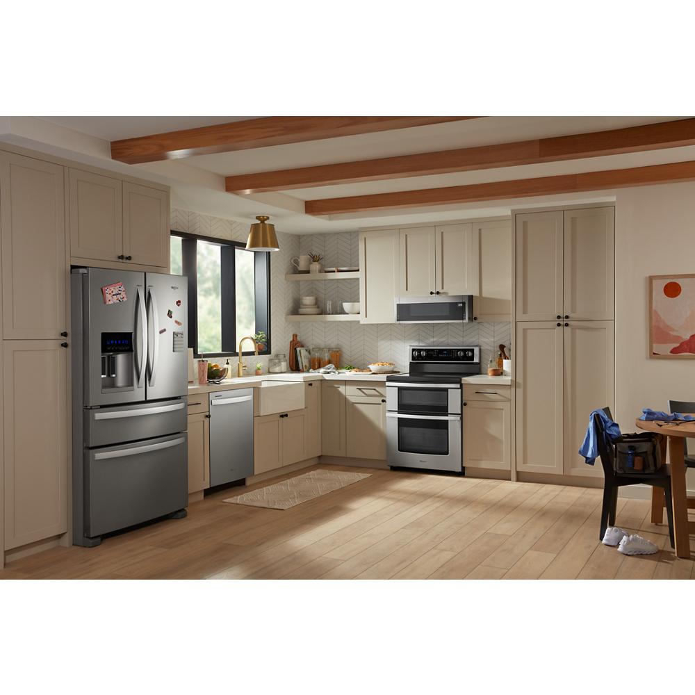Kitchen with beige cabinets, stainless steel appliances, including electric double oven range and dishwasher near window