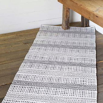 Black and white geometric pattern runner rug on wooden floor under rustic wooden bench for home decor